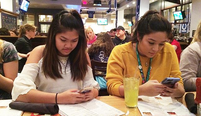 Junior Hannah Nguyen and senior Liza Fortozo check social media during dinner at Rock Bottom on Saturday, Nov. 12. The convention attendees went to multiple sessions on the convention, followed by a sponsored student dance. Photo by Madi Calvert. 