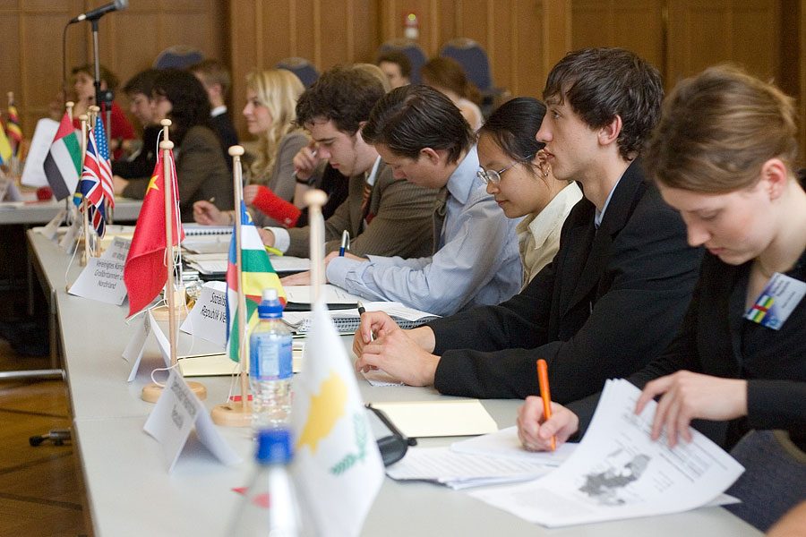 Model United Nations members from a school in Germany attend a meeting. Delegates in the committee either use nameplates or small flags to represent which country they speak for in the committee chamber. 