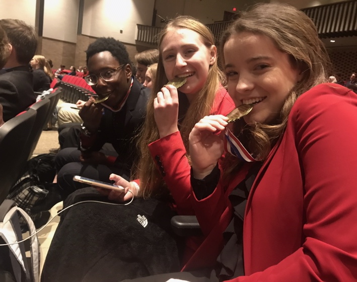 Former+2019+graduates+Abidemi+Aregbe%2C+Callie+Johnson+and+Maddie+Butler+bite+on+their+first+place+medals+for+the+World+Schools+event+for+debate+at+Southport+High+School+on+Jan.+26%2C+2019.