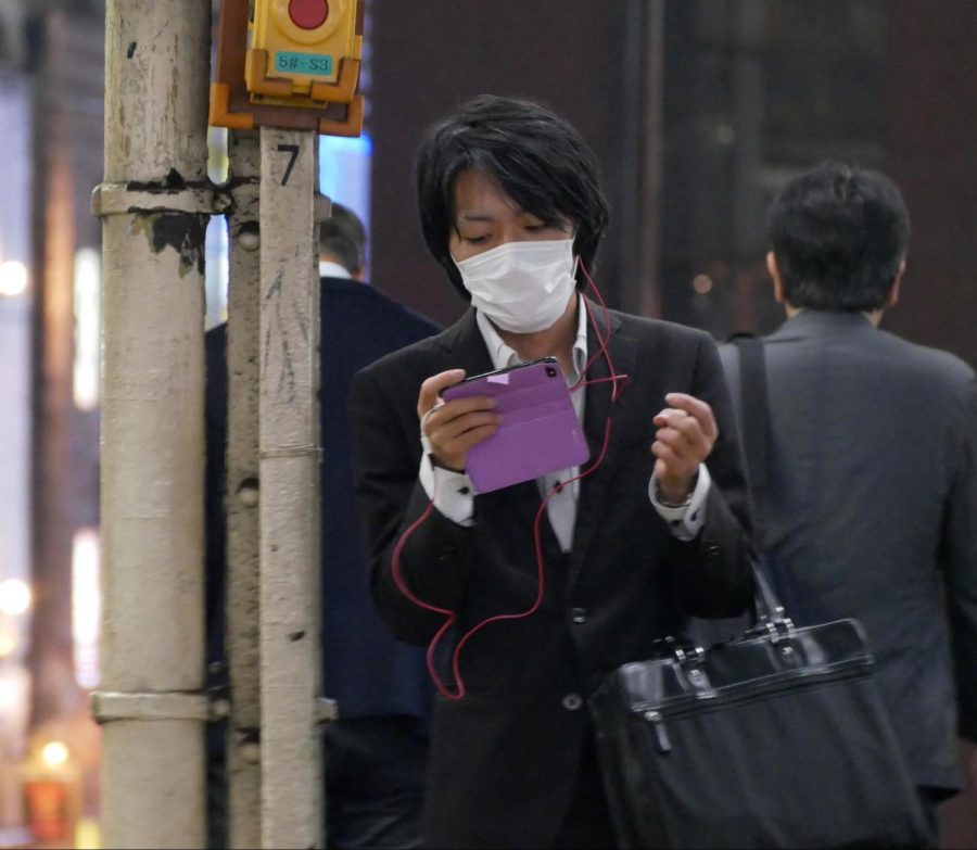 Tokyo man wears a courtesy mask while reading his phone.