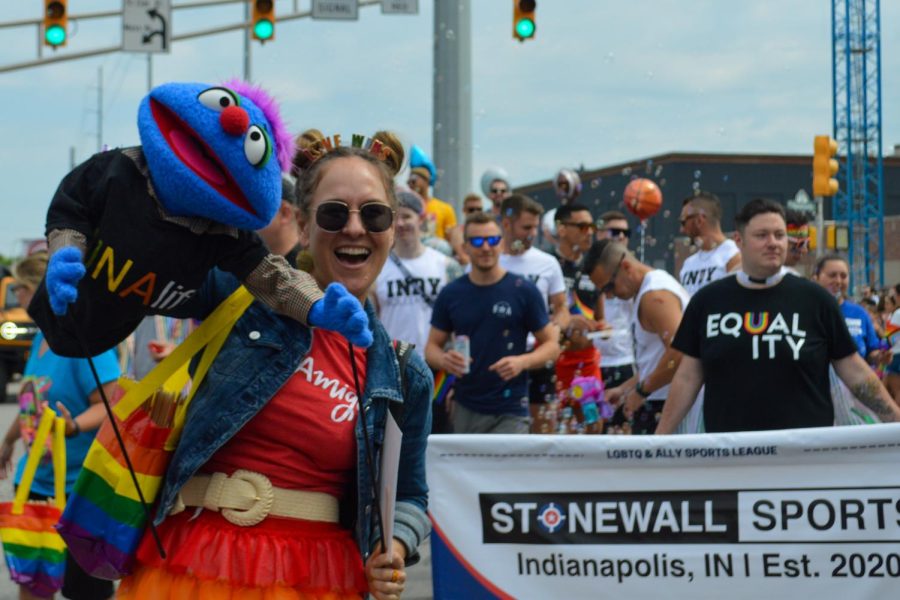 A ventriloquist and puppet smile with the crowd as Stonewall Sports awaits their turn to begin marching.