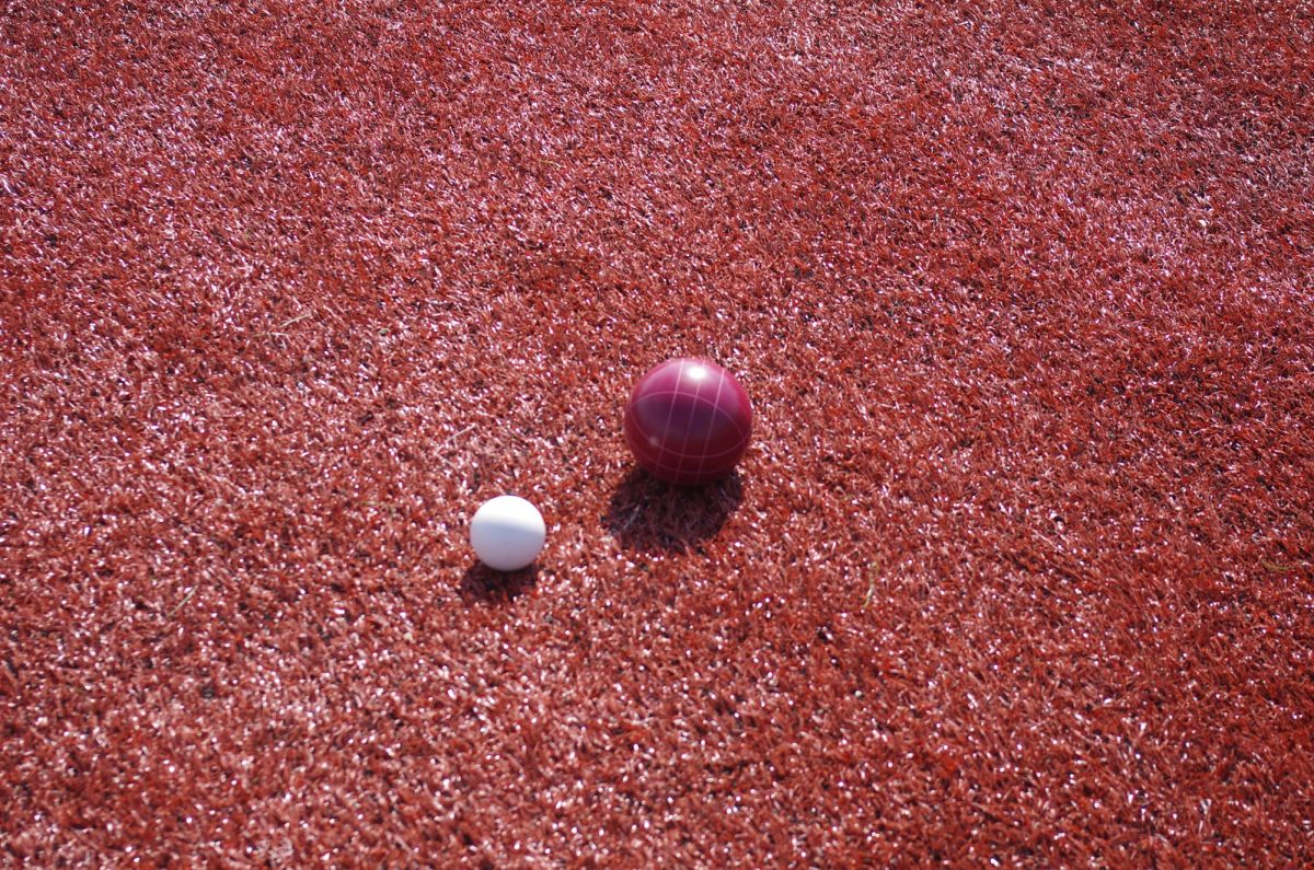 A red ball belonging to Fishers High School sitting close to the white Bocce ball. The red ball won FHS two points.