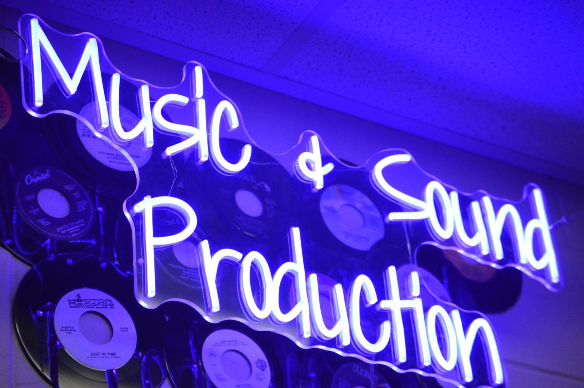 A neon sign that says “Music and Sound Production” with vinyl records behind it. Photo by Addy Davis.
