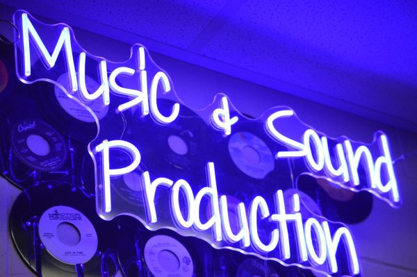 A neon sign that says “Music and Sound Production” with vinyl records behind it. Photo by Addy Davis.