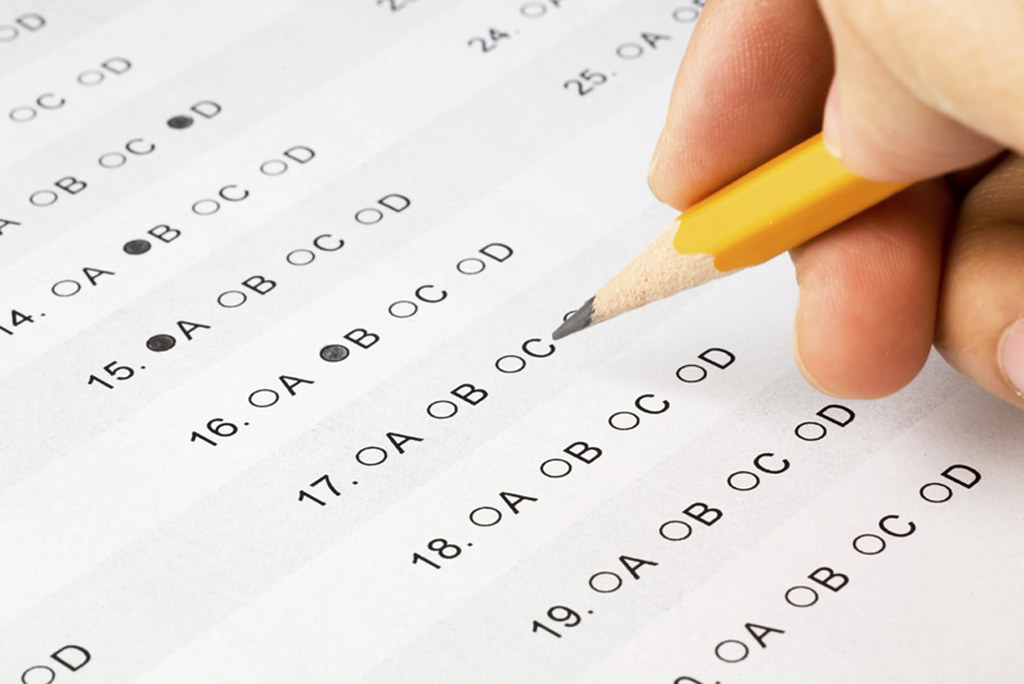 A student holds a pencil while deliberating over answer choices in a multiple choice test. Photo courtesy of creative commons.
