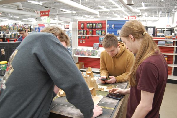Junior Kyle Chapman [middle, brown hooded sweatshirt], and his friends Jacob Grogan [left, gray sweatshirt] and Coda Cyders [right] set up tournament pairings at HobbyTown in Indianapolis on March 14. Chapman is directing the tournament. He is in cooperation with Third Phase Incorporated, an organization focused on helping those in need. All funds raised go towards creating homeless kits and are sent directly to Third Phase Incorporated upon completion of his project. 
