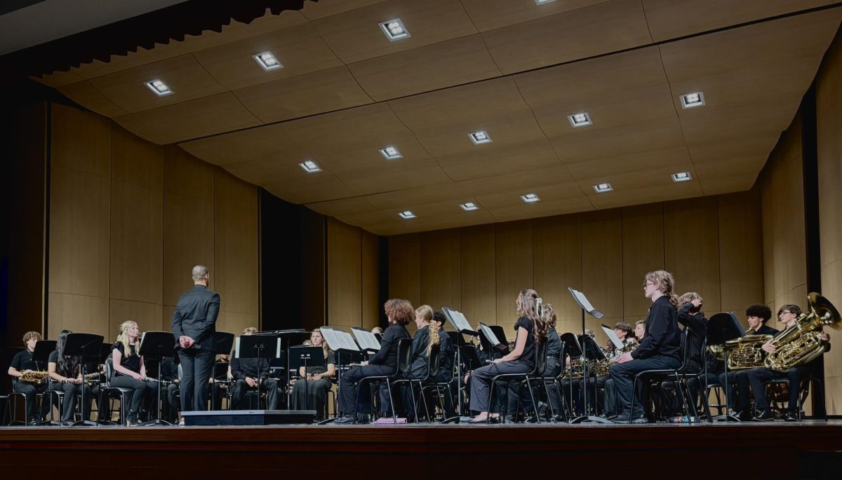 Symphonic White band anticipates the beginning of their performance. Director Nico Johnson stands at the side of the podium, ensuring every musician is in place before bringing the ensemble to set. 