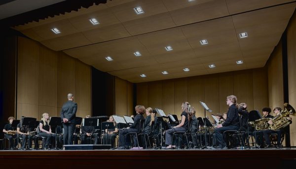 Symphonic White band anticipates the beginning of their performance. Director Nico Johnson stands at the side of the podium, ensuring every musician is in place before bringing the ensemble to set. 